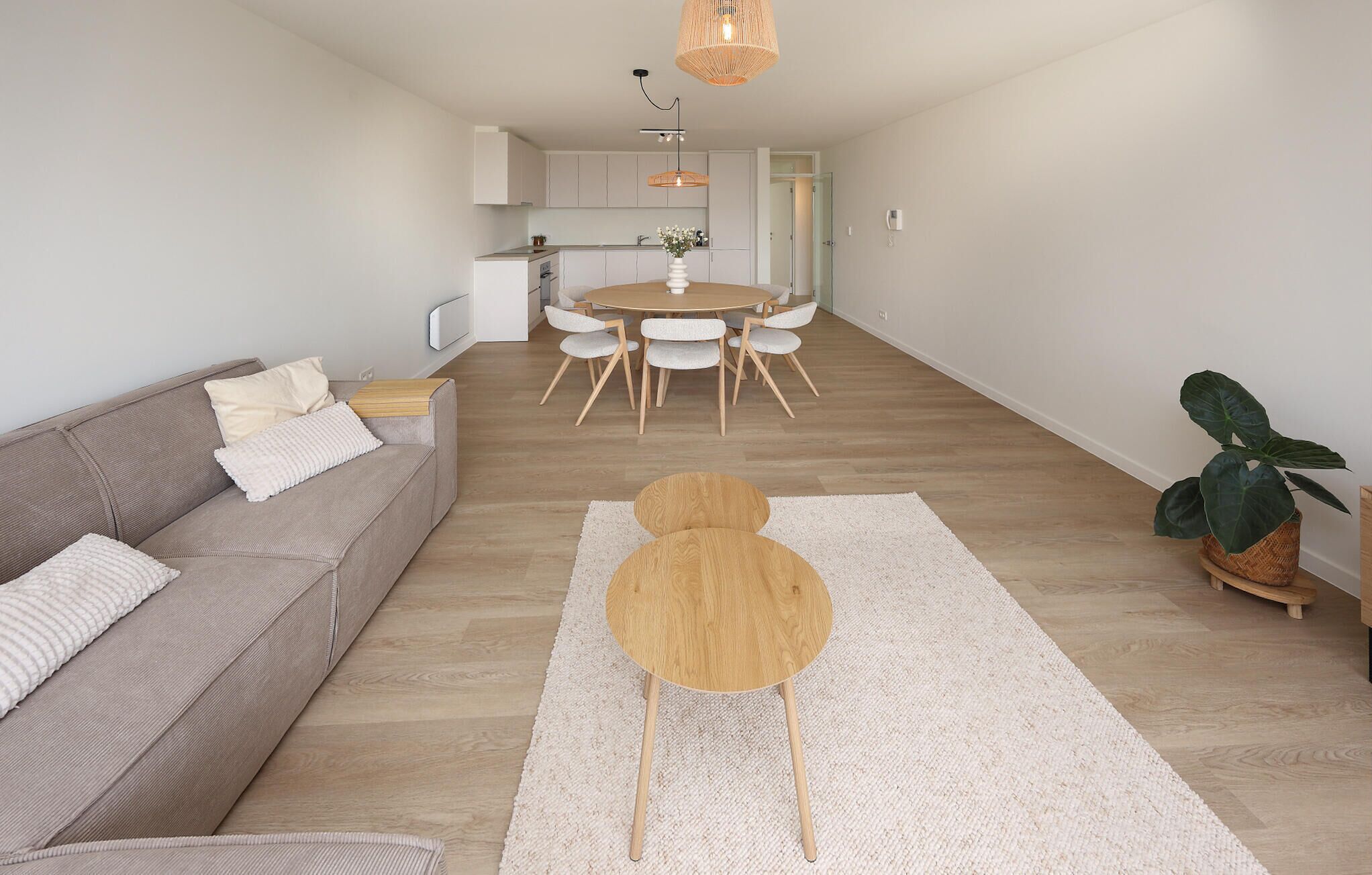 A modern living room with a sofa, a round wooden coffee table, and a dining area with a round table and chairs.