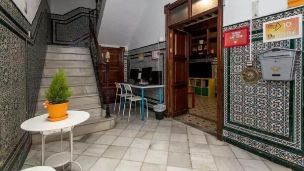 A narrow hallway with a tiled floor, a small table with a potted plant, and a staircase with a wooden railing. - Apartamentos Arc House (Seville)