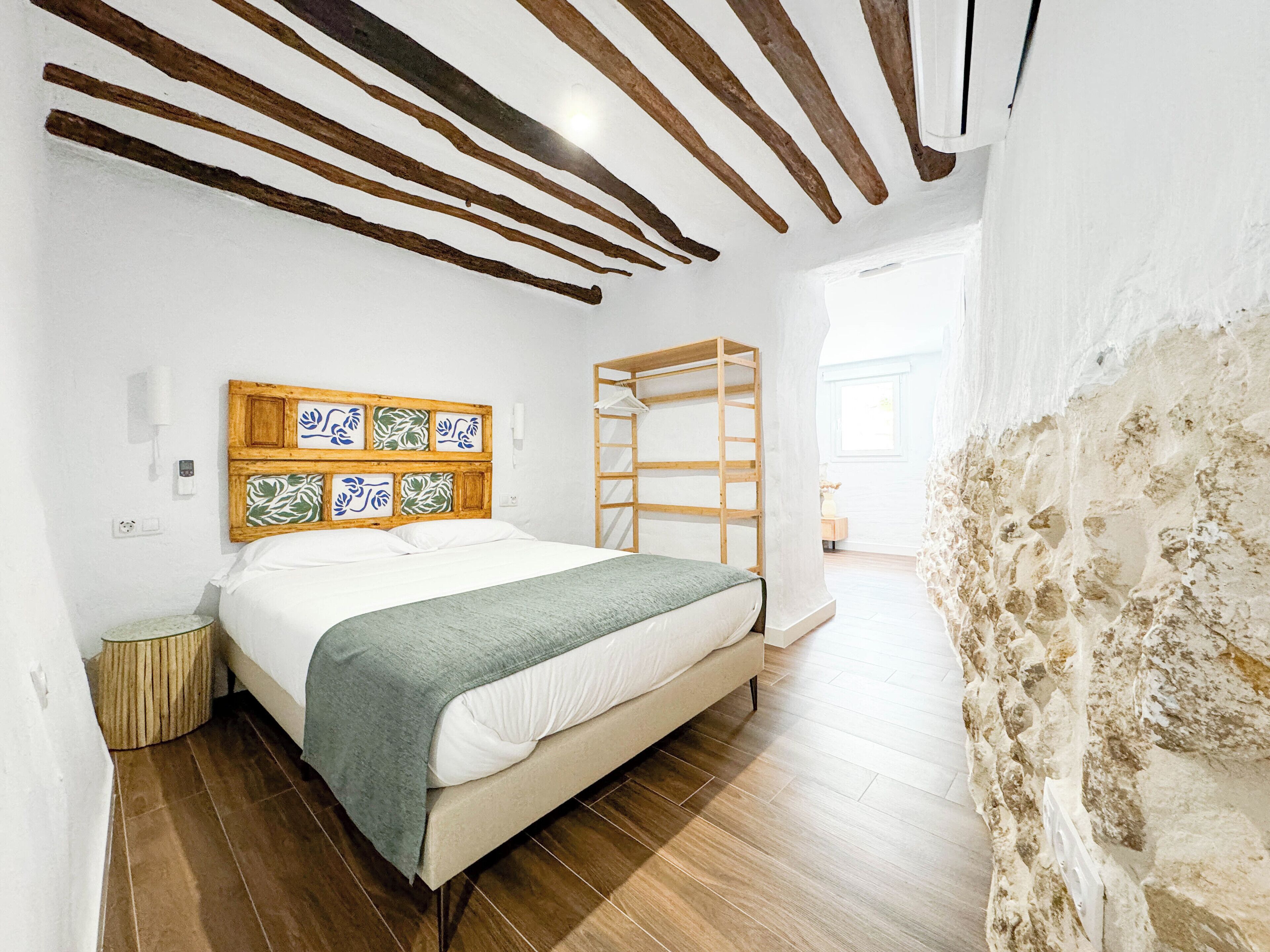 A bedroom with a wooden headboard, a bed with a green blanket, a wooden ladder, and a stone wall.