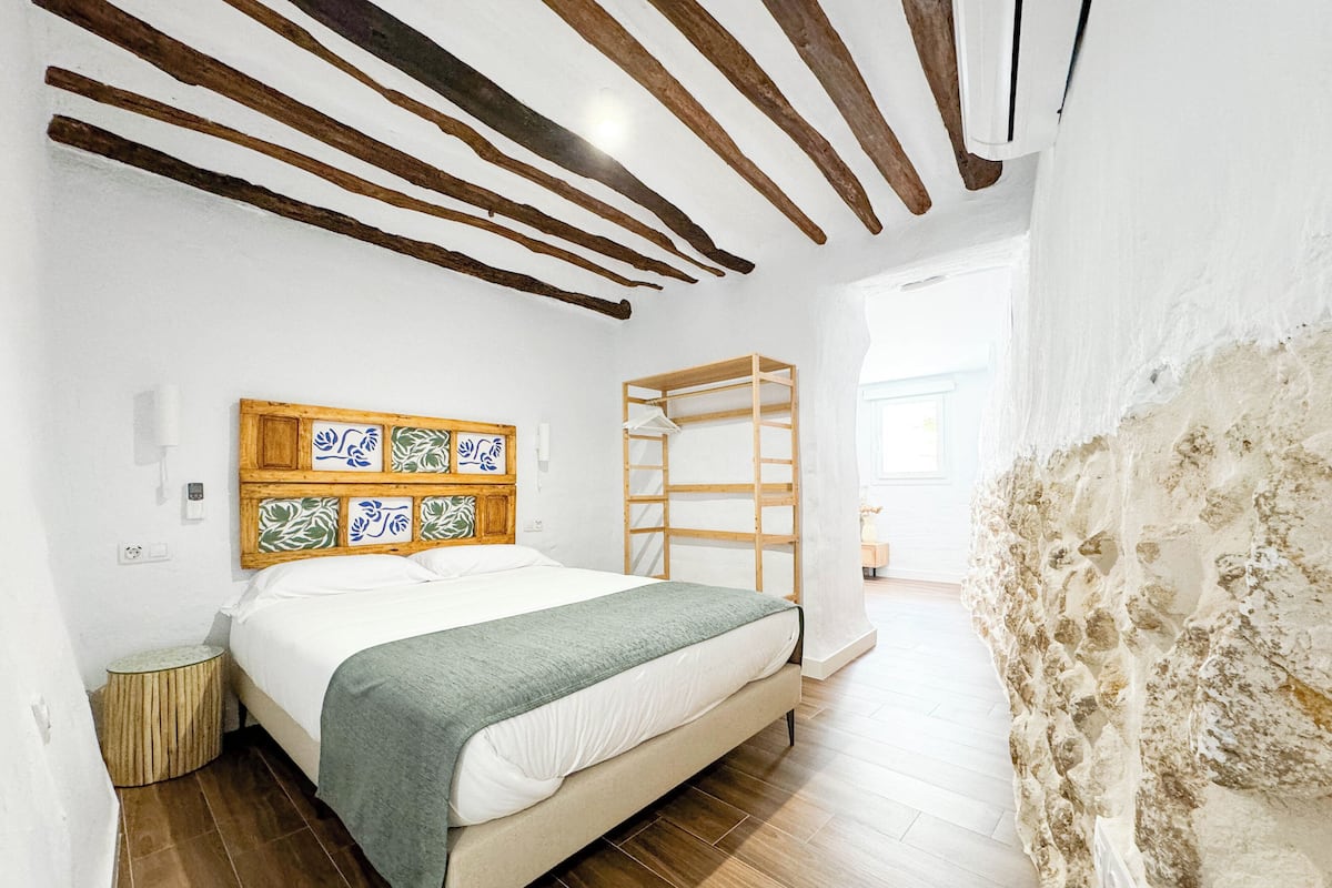 Ein Schlafzimmer mit einem Holz-Kopfteil, einem Bett mit grüner Decke, einer Holzleiter und einer Steinwand.