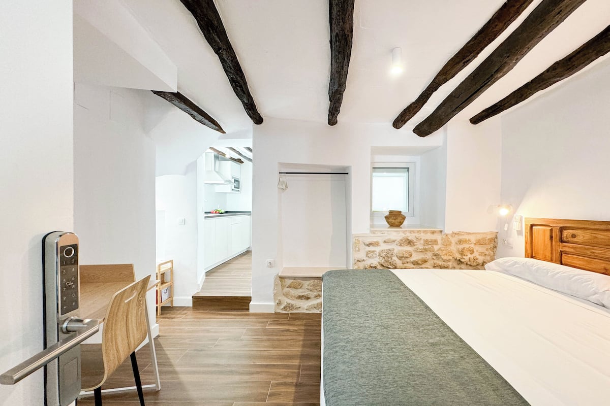 Ein Schlafzimmer mit Bett, Schreibtisch, Stuhl und Blick auf eine Küche und ein Badezimmer.