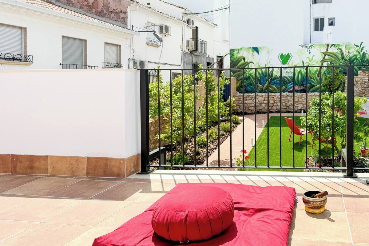 A red cushioned seating area on a tiled patio with a view of a garden and a mural on a building wall.