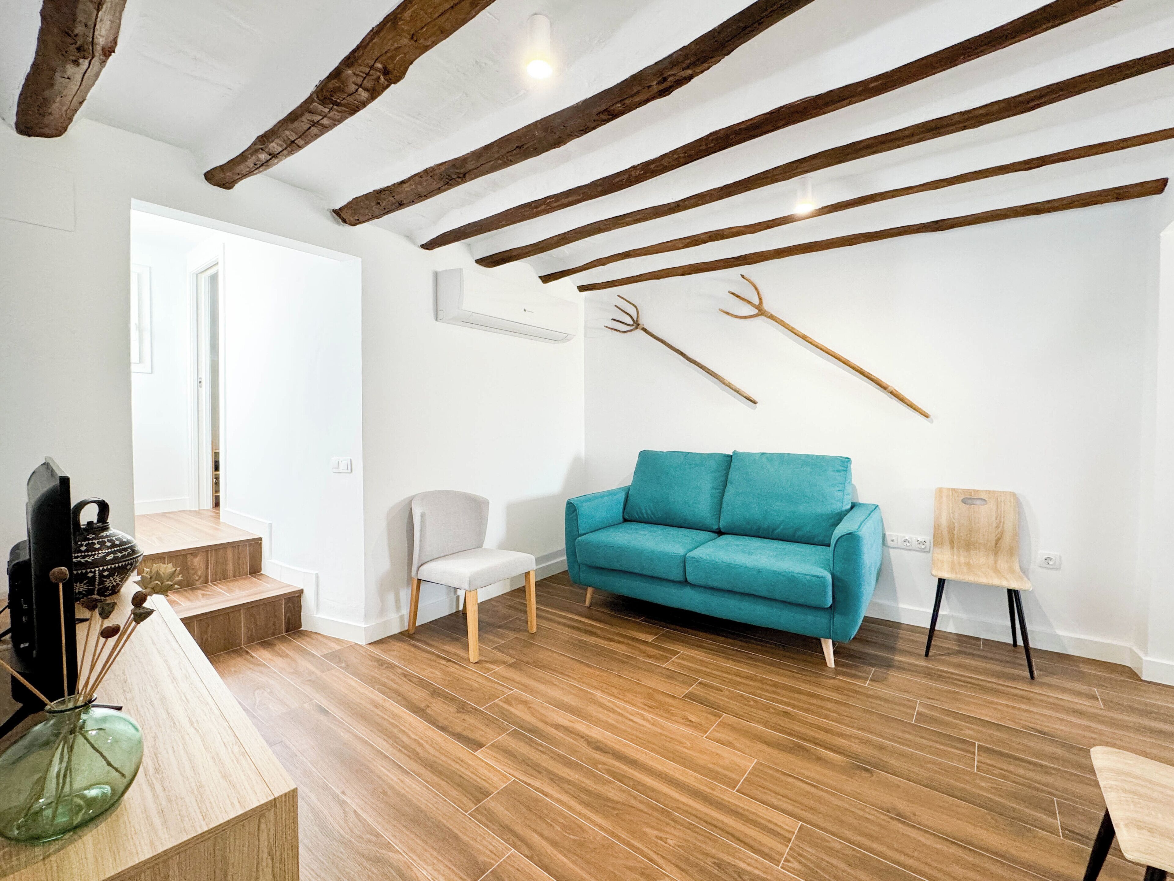 A modern living room with a teal sofa, wooden flooring, exposed beams, and rustic decor.