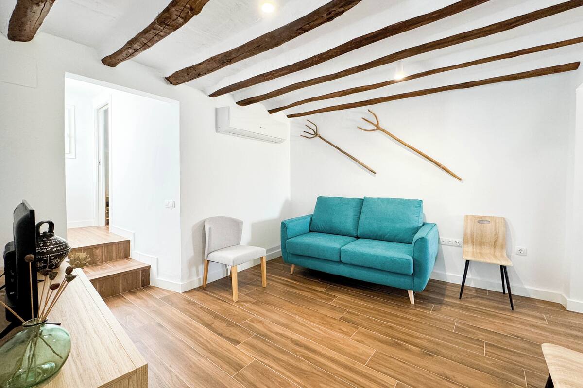 A modern living room with a teal sofa, wooden flooring, exposed beams, and rustic decor.