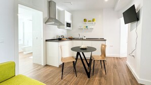 Eine moderne Küche mit weißen Schränken, einer Mikrowelle und einer Edelstahl-Dunstabzugshaube. Ein Esstisch mit Stühlen und ein an der Wand befestigter Fernseher sind ebenfalls vorhanden.