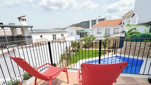 Ein Balkon mit roten Stühlen, einem Schwimmbad und Blick auf umliegende Häuser.
