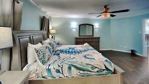 A bedroom with a bed, a dresser, a mirror, a ceiling fan, and a window. - Harbor View Breeze by Ryson Vacation Rentals (Galveston)