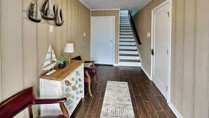 A hallway with wooden flooring, a staircase, a door, and a small table with a lamp and decorative items. - Harbor View Breeze by Ryson Vacation Rentals (Galveston)