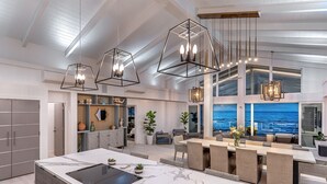 Una cocina amplia con una isla de mármol, elegantes lámparas colgantes y vistas al océano a través de grandes ventanales.