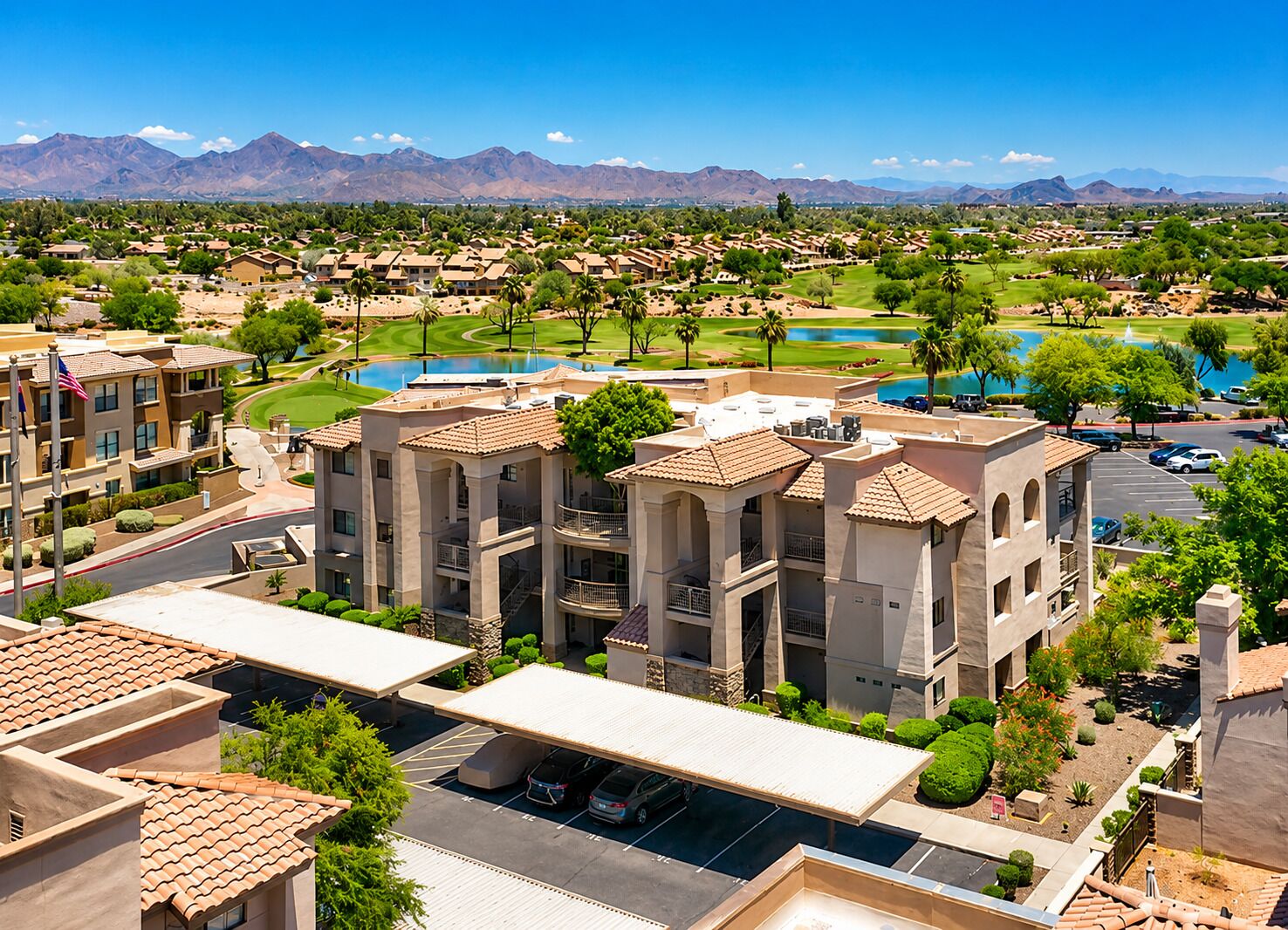 Un hotel de varios pisos con piscina en la azotea, campo de golf y montañas al fondo.