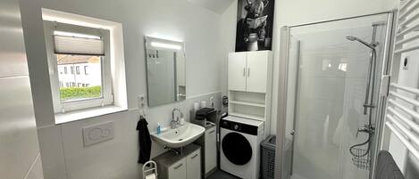 A modern bathroom with a window, a sink, a mirror, a toilet, a washing machine, and a shower.