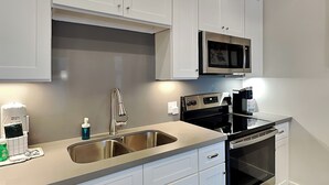 A modern kitchen with stainless steel appliances, a double sink, and white cabinetry. - Tremont Meilleur 104 by Ryson Vacation Rentals (Galveston)