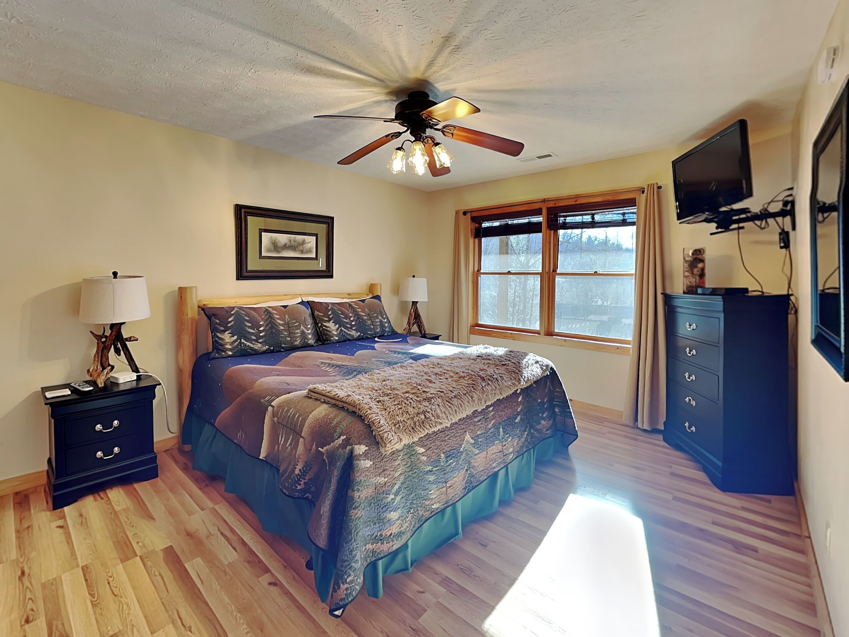 Une chambre à coucher avec un lit, un ventilateur de plafond, une fenêtre, une commode et un téléviseur.