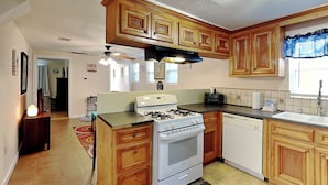 A kitchen with wooden cabinets, a gas stove, a dishwasher, and a ceiling fan. - Sugar Shack Bungalow by Ryson Vacation Rentals (Galveston)