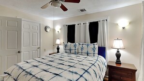 A bedroom with a bed, a nightstand, a dresser, a ceiling fan, and a wall clock. - Sugar Shack Bungalow by Ryson Vacation Rentals (Galveston)