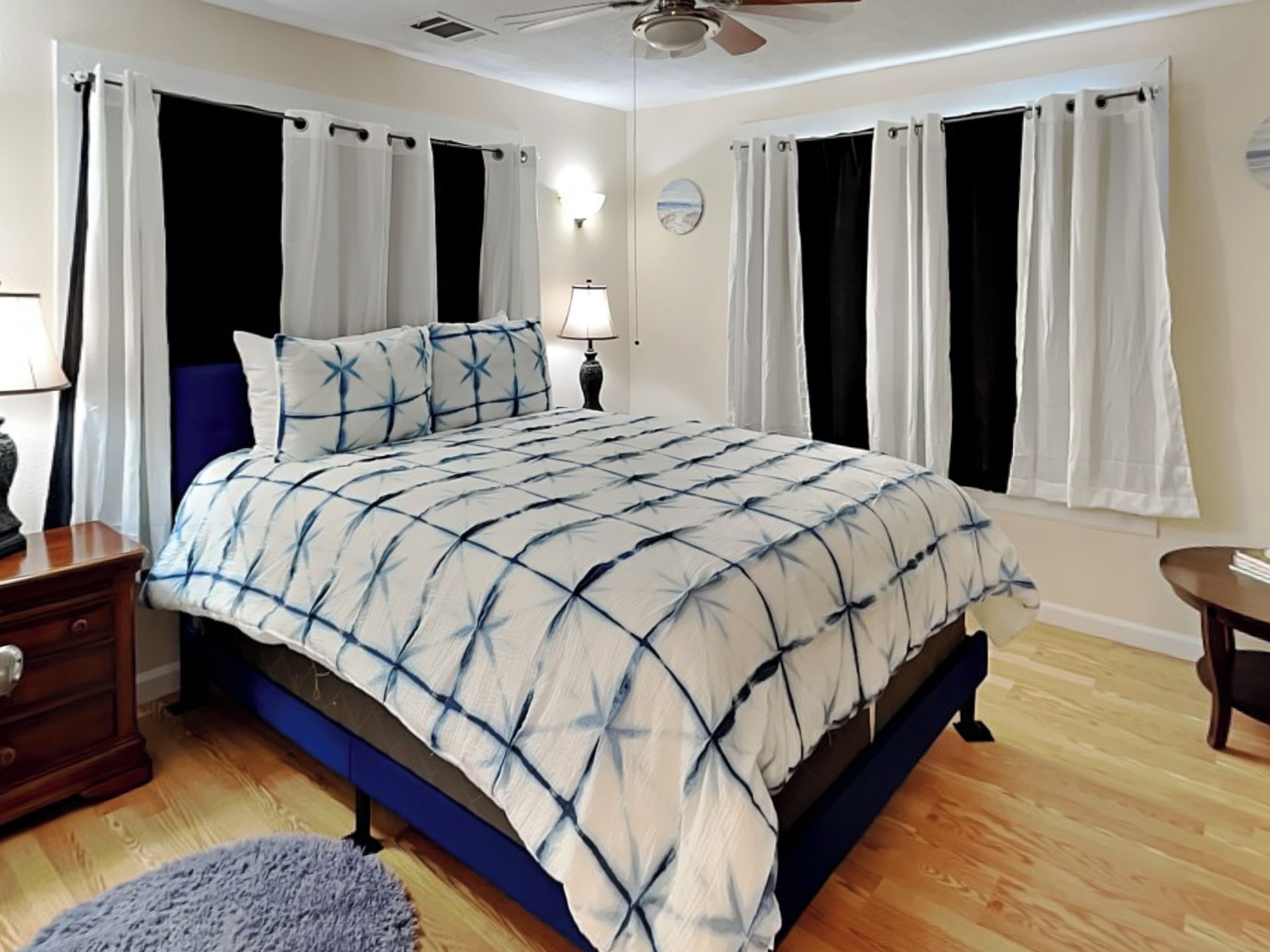 Quarto com cama, cortinas, mesa de cabeceira, luminária e uma pequena mesa.