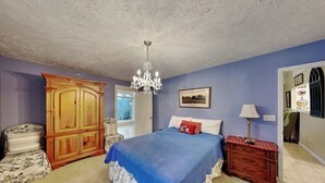 Un dormitorio con una cama grande, una araña, un armario de madera, una silla y un aparador.