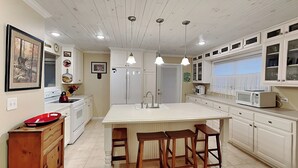 Una cocina con isla central, muebles blancos e iluminación colgante.