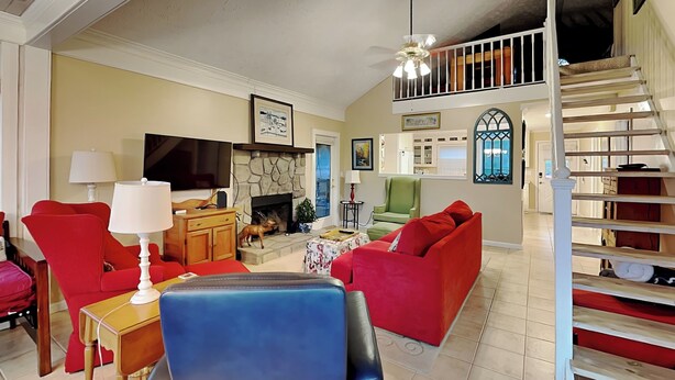 Una sala de estar con chimenea, sofás rojos, un sillón azul y una escalera.