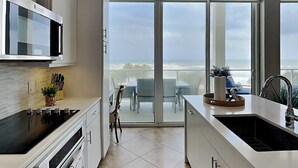 A modern kitchen with a large island, a microwave, and a view of the ocean through large sliding glass doors. - Endless Summer by Ryson Vacation Rentals (Galveston)