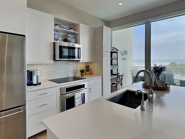 A modern kitchen with a large island, stainless steel appliances, and a view of the ocean through a large window.