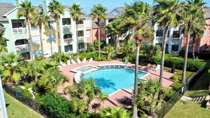 A pool surrounded by palm trees and a multi-story building with balconies. - First Light by Ryson Vacation Rentals (Galveston)