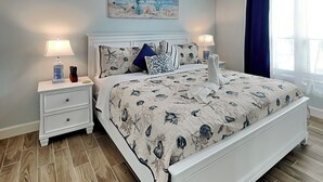 A bedroom with a bed, nightstands, a painting, and a window with curtains. - First Light by Ryson Vacation Rentals (Galveston)