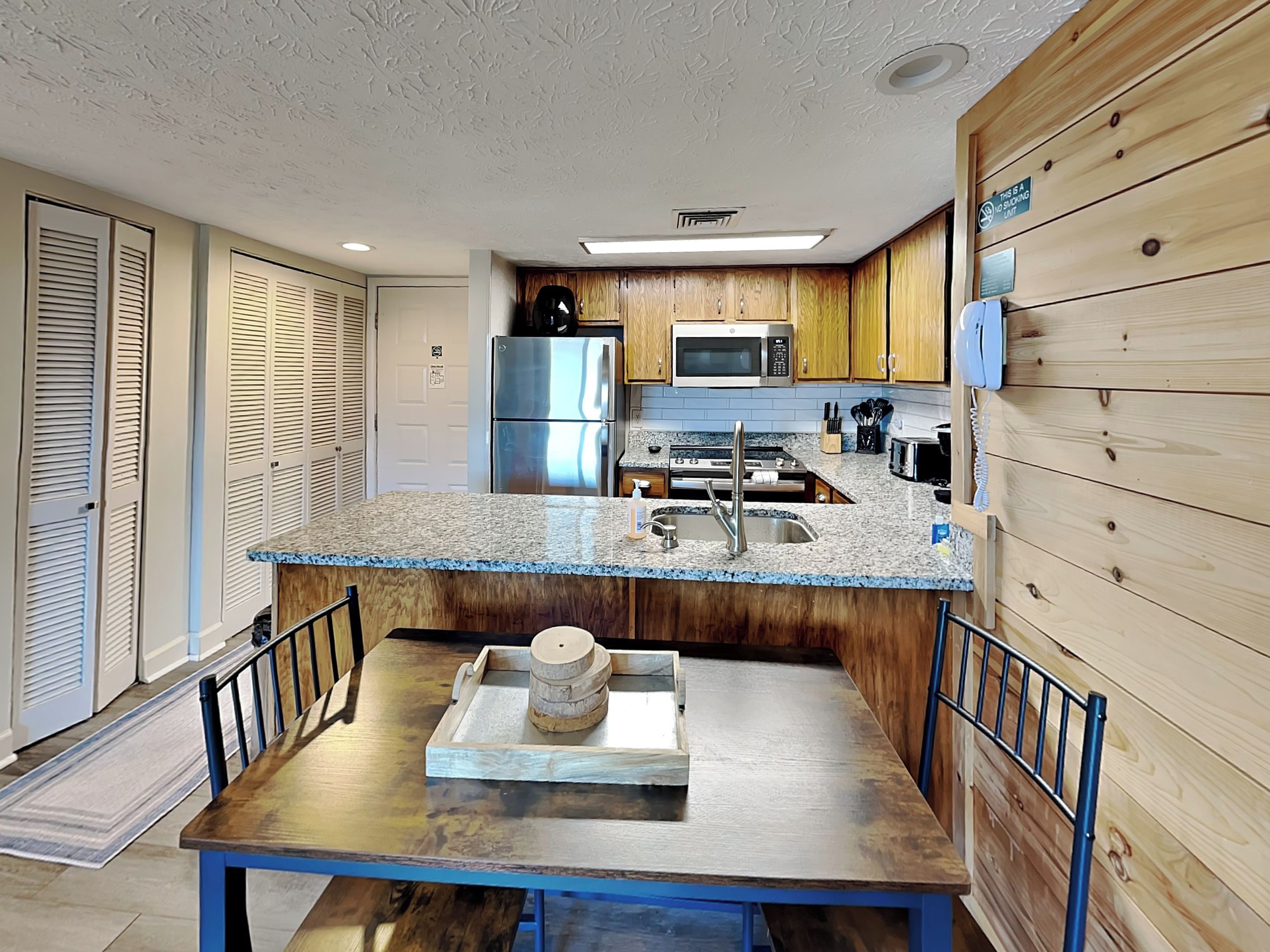 A modern kitchen with wooden cabinets, a stainless steel refrigerator, a microwave, and a granite countertop.