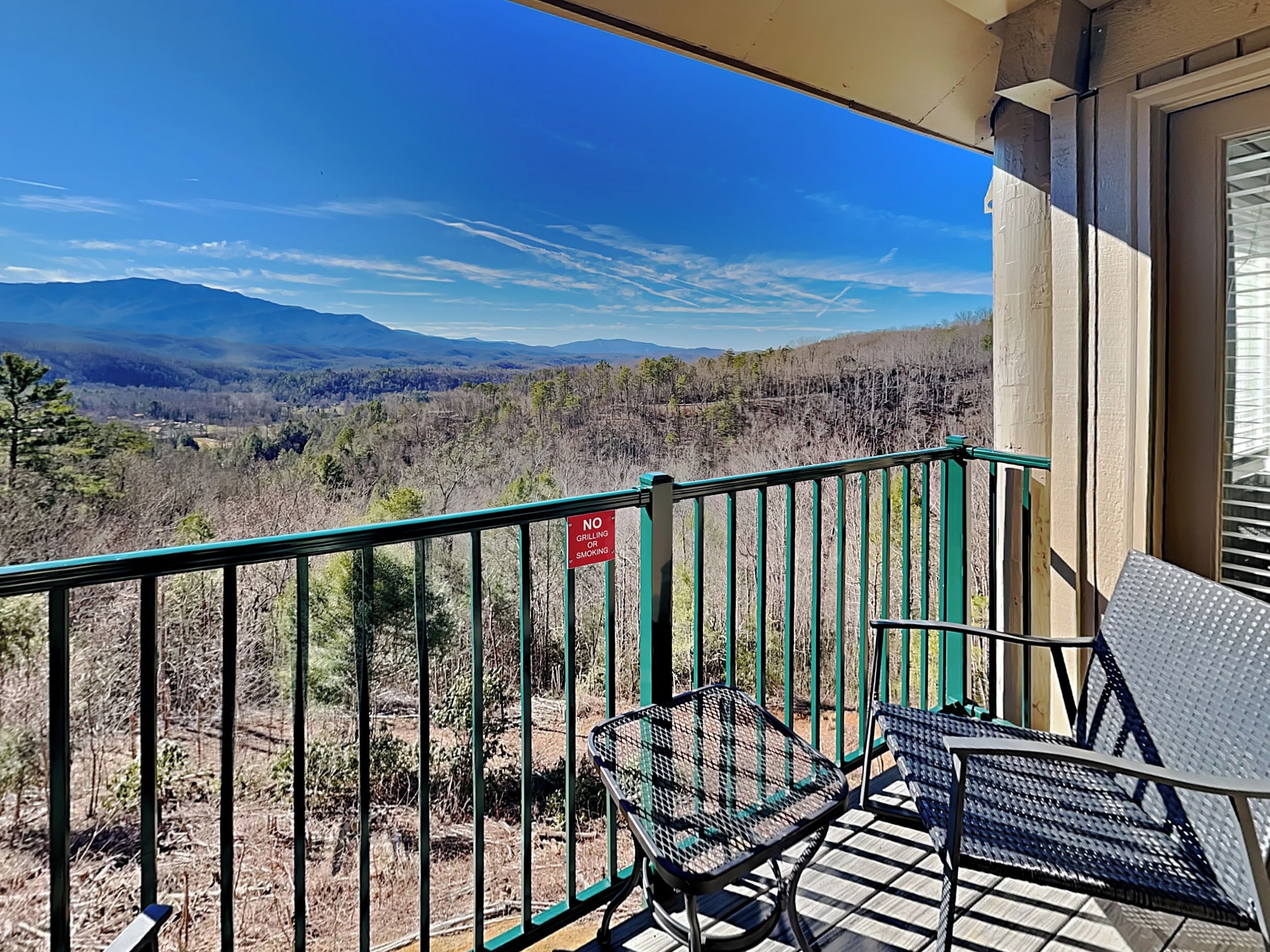 Un balcon avec vue sur les montagnes, un panneau indiquant qu’il est interdit de faire des barbecues ou de fumer, et du mobilier d’extérieur.