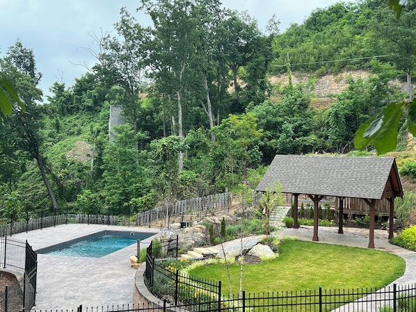 A pool surrounded by a black metal fence, a wooden gazebo, and a well-maintained lawn.