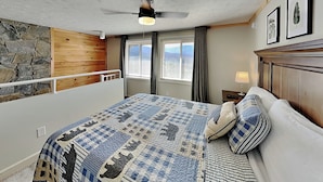 A bedroom with a bed, a ceiling fan, a window with curtains, and a stone wall.