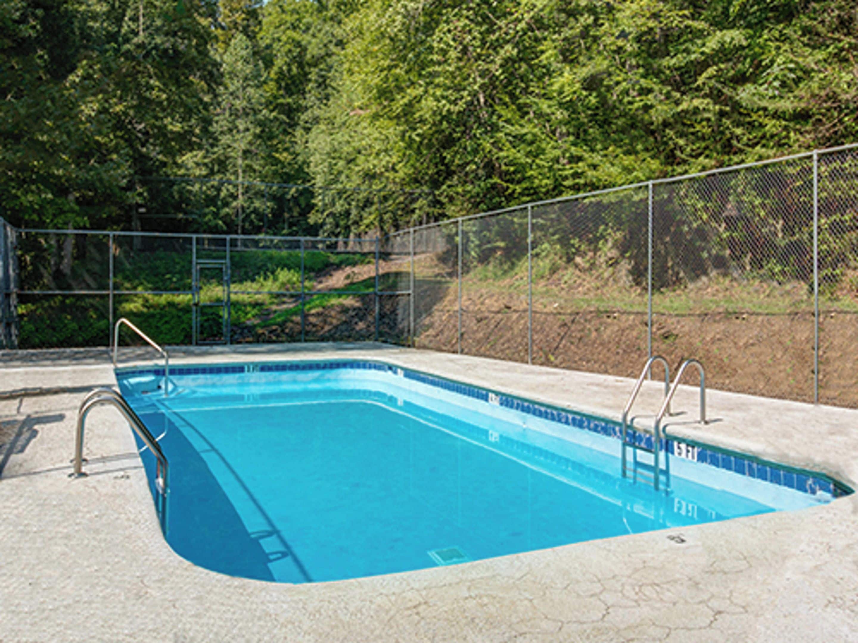 A rectangular swimming pool with a blue interior, surrounded by a metal fence and concrete deck.