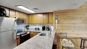 A kitchen with wooden cabinets, a stainless steel refrigerator, a microwave, a toaster, and a sink.