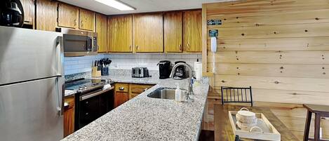A kitchen with wooden cabinets, a stainless steel refrigerator, a microwave, a toaster, and a sink.