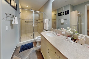 Un baño moderno con ducha envuelta en vidrio, un lavabo grande y un espejo con una planta decorativa.