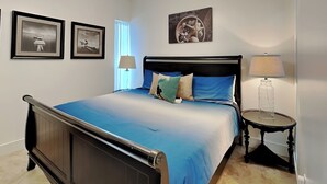 Un dormitorio con cama, dos lámparas de noche, una mesita de noche y cuadros en la pared.