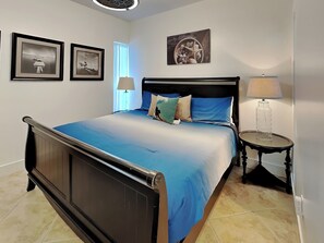 Un dormitorio con cama, dos lámparas de noche, una mesita de noche y cuadros en la pared.