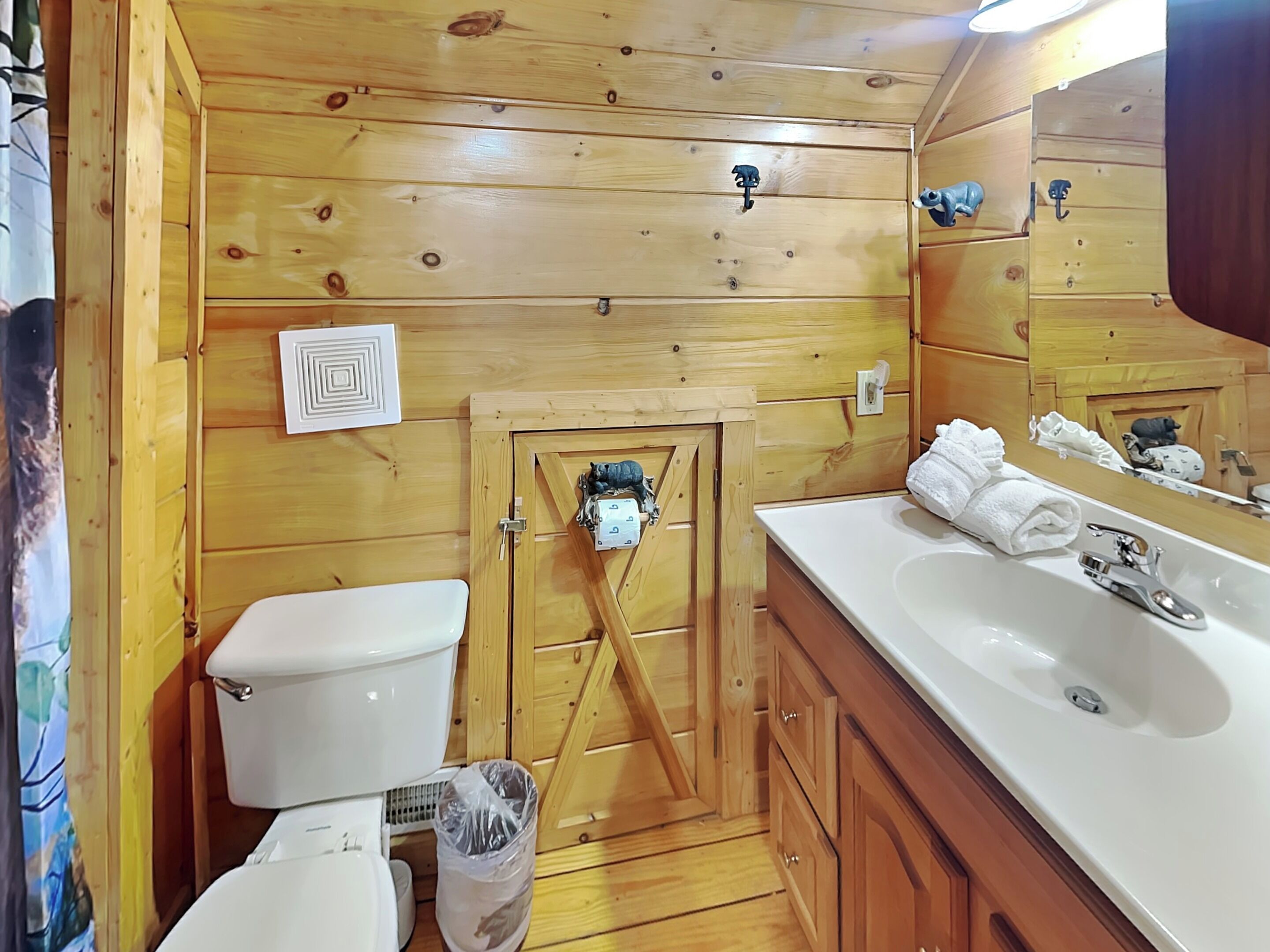 A wooden cabin bathroom with a toilet, sink, and wooden cabinets.