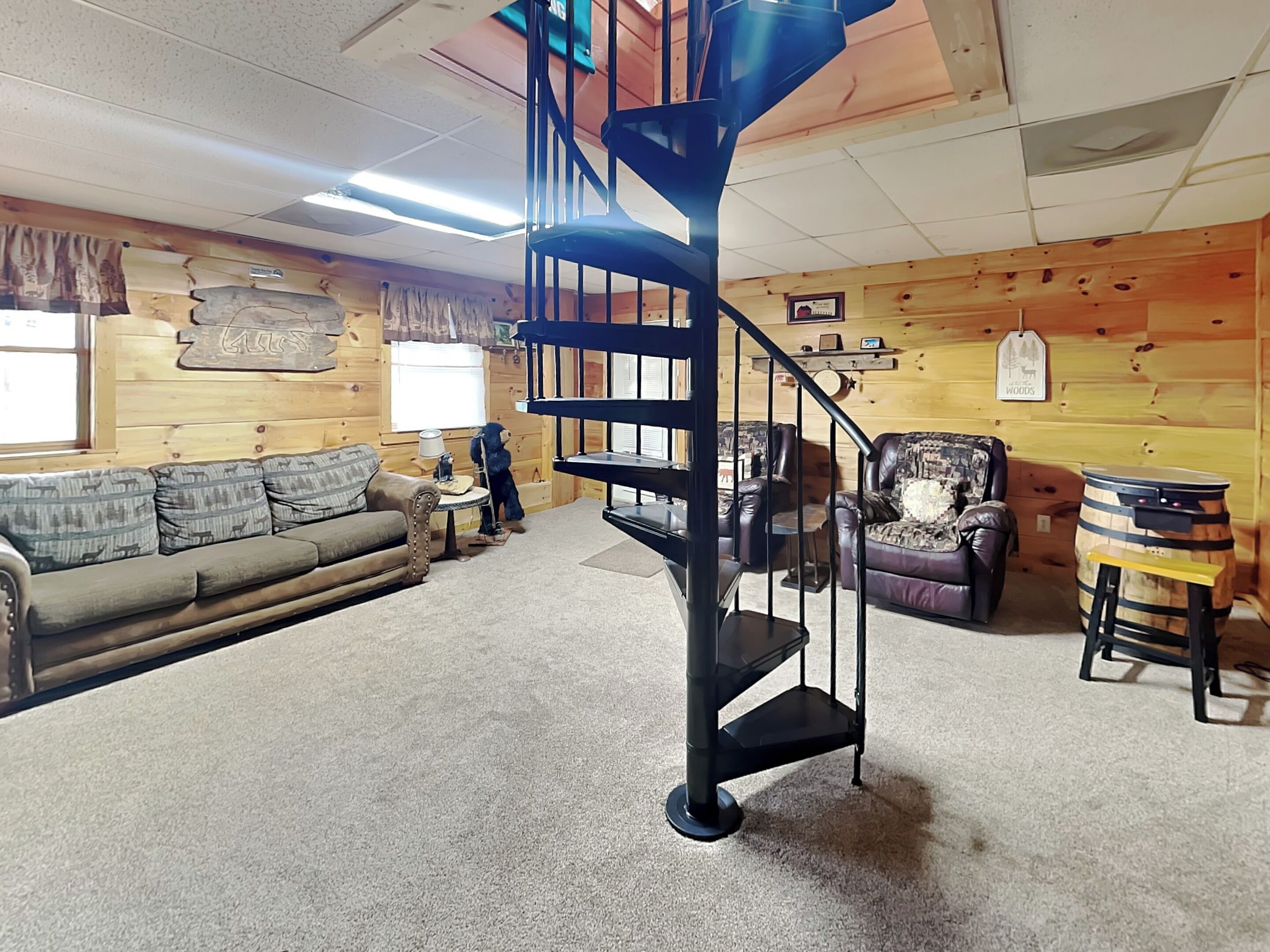 A cozy living room with a wooden interior, a black spiral staircase, a sofa, a chair, and a drum.