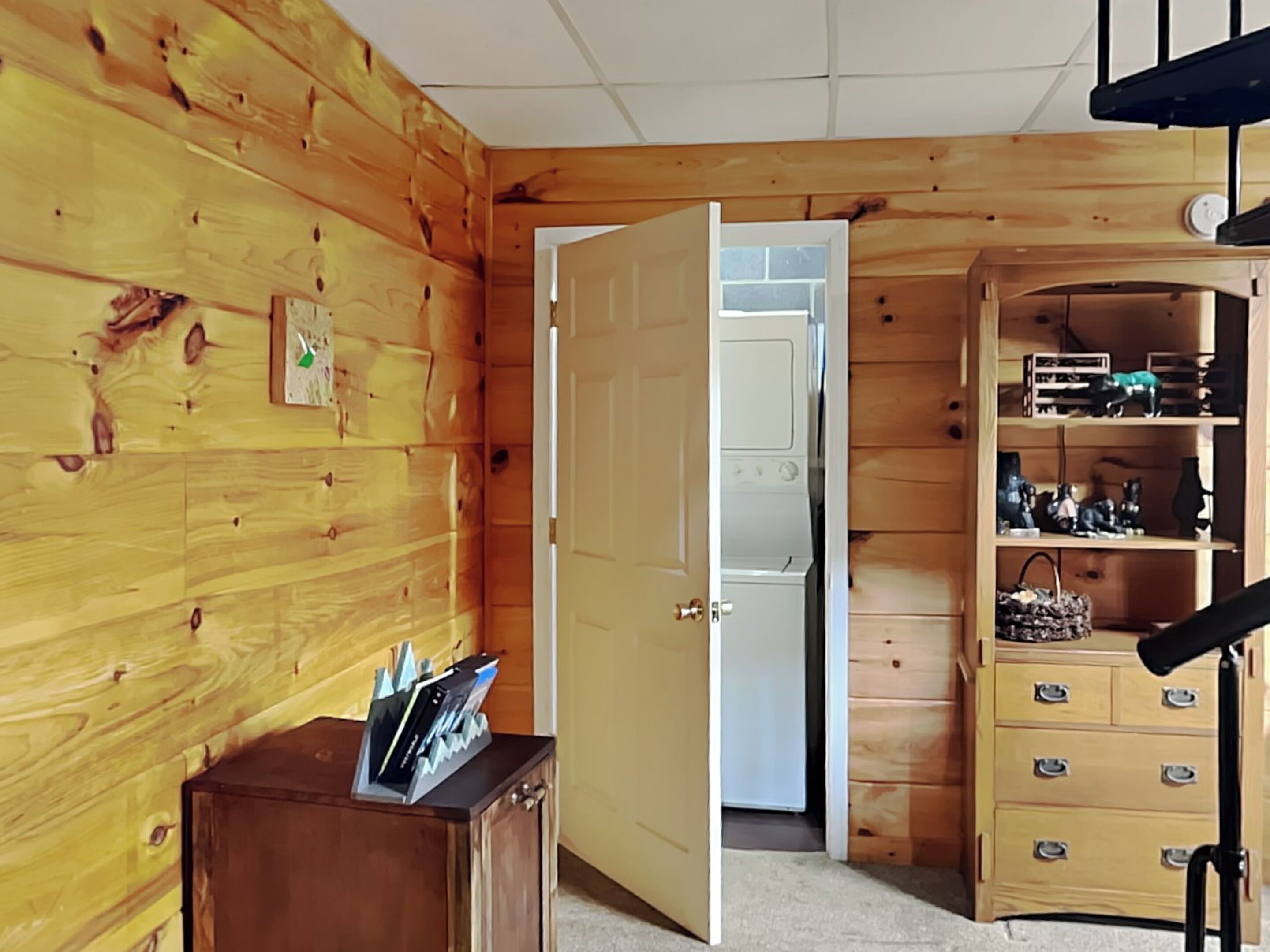 A wooden-paneled room with a wooden cabinet, a door leading to another room, and a shelf with various items.