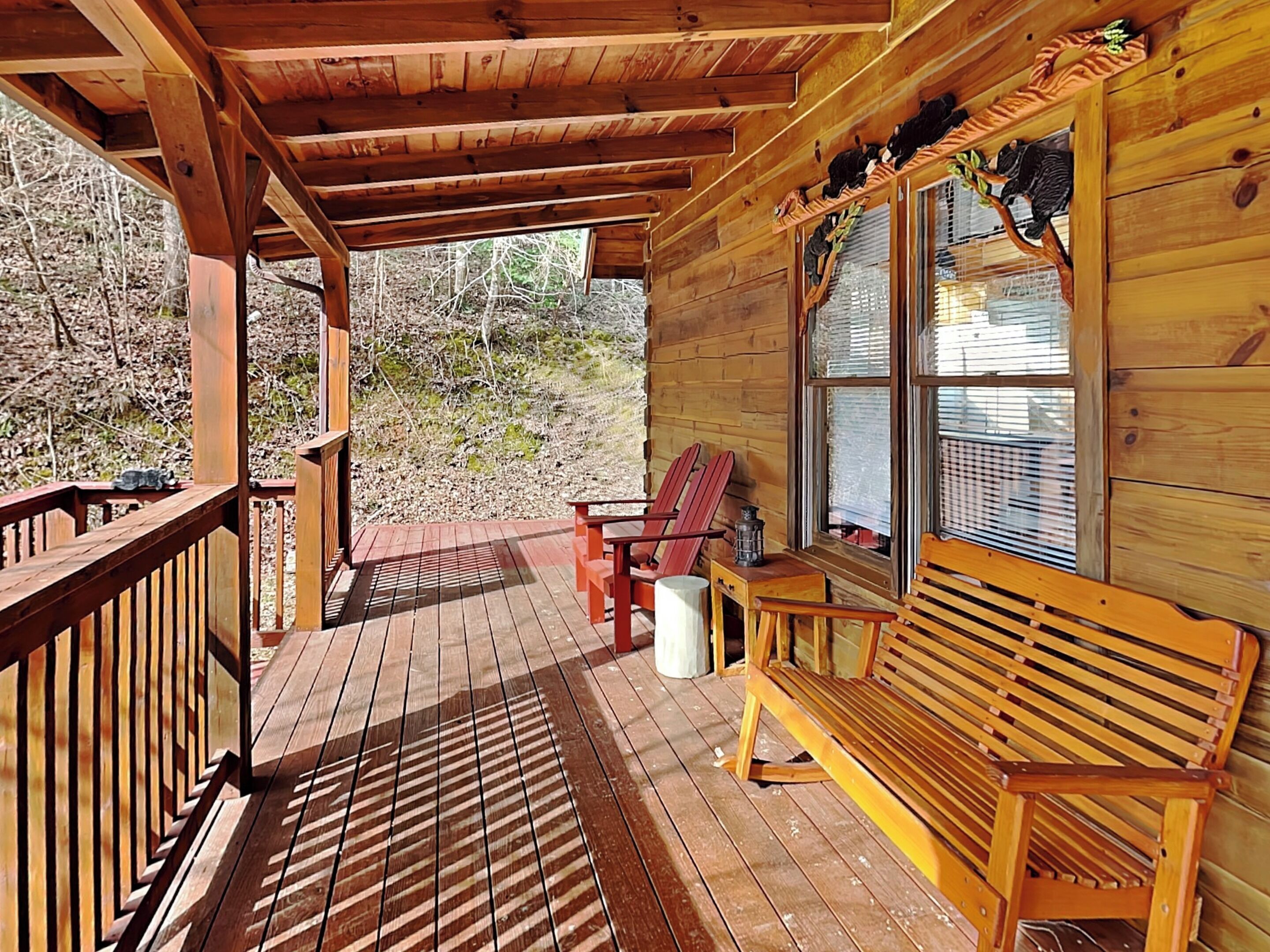 Una cabaña de madera con un porche, un banco y dos sillas Adirondack.