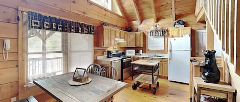 A wooden cabin with a kitchen area, a dining table, and a bench.