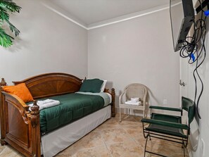 A bedroom with a wooden bed, a green bedspread, a white chair, and a small table. - Western Waves by Ryson Vacation Rentals (Galveston)