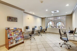 A modern office space with a bulletin board, multiple workstations, and large windows.