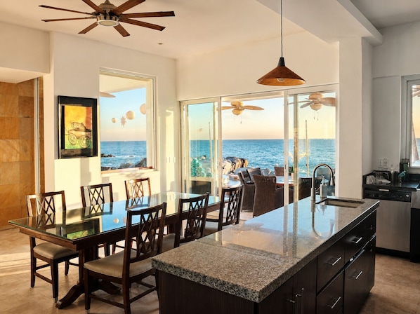 Una cocina moderna con una isla grande, un comedor con sillas y vistas al océano.