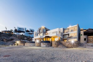 A modern multi-story building with a stone facade, large windows, and outdoor lighting.