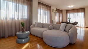 A modern living room with a large L-shaped sectional sofa, a round coffee table, and a dining area with a table and chairs.