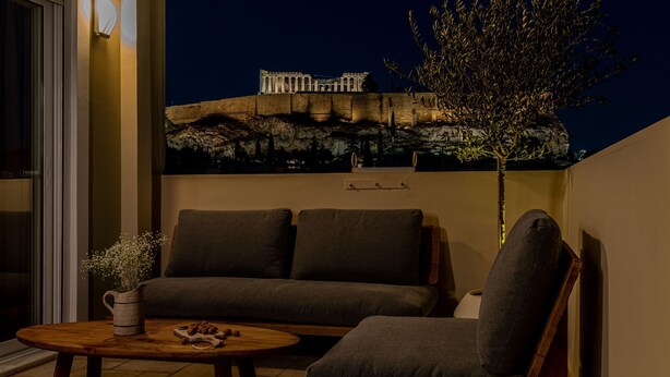 A balcony with a sofa, armchair, and coffee table, overlooking a historic building at night.