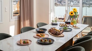 A dining table with various dishes and drinks, set in a room with large windows overlooking a cityscape.