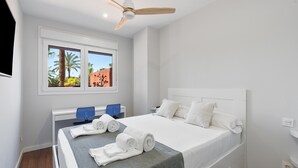 A bedroom with a bed, a ceiling fan, a window with a view of palm trees, and a TV mounted on the wall. - Ref. 565600 (Motril)